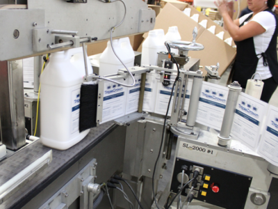 A processing plant showing automated machine attaching labels to a packaging container.